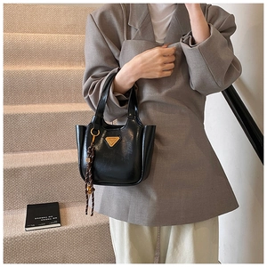 Detail of black glossy handbag with golden triangle plaque and woven tassel charm
