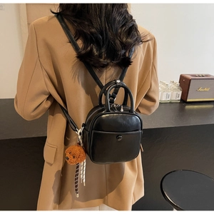 Detail of a black mini square bag with a brown plush bear charm and silver double zippers