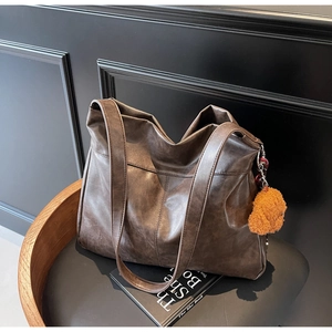 Detail of a large dark brown tote bag with a plush bear charm on a vintage chair