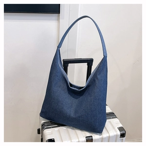 Détail du grand sac cabas en denim bleu suspendu à la poignée d'une valise blanche