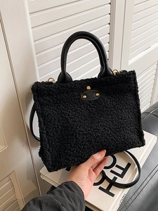 Large black plush tote bag with leather handles and gold studs on a minimalist sofa