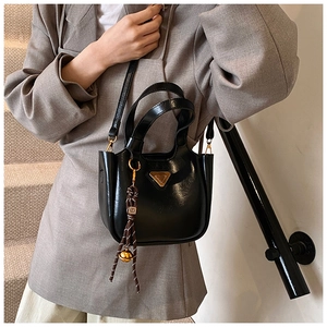 Detail view of the sleek black bucket bag with a golden tassel charm and metal logo
