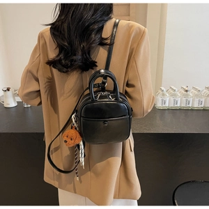 Detail of a black mini backpack with top handle and a brown plush teddy bear charm