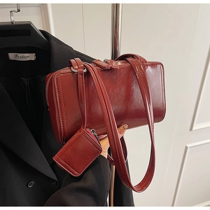 Macro detail of wine red glossy leather shoulder bag with adjustable strap and small charm pouch