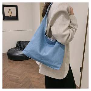 Détail d'un grand sac cabas minimaliste en toile denim porté à l'épaule par un mannequin