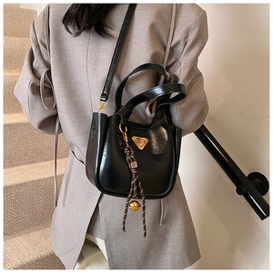 Detail of black glossy bucket bag featuring gold triangle logo and braided rope charm