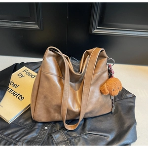 Detailed texture of brown faux leather tote bag with a plush teddy bear charm accessory