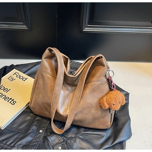 Brown leather tote bag detail with cute teddy bear plush charm on a vintage leather jacket
