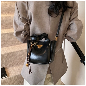 Detail of black glossy bucket bag featuring gold triangle logo and woven bell charm