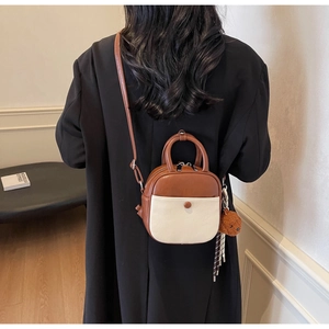 Detail of a brown and beige leather mini bag with a teddy bear charm and strap