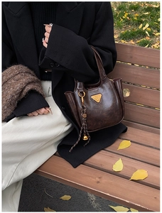 Detail of dark brown leather bucket bag with gold triangle emblem on wooden bench
