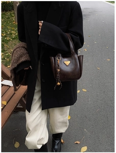 Detailed close-up of dark brown vintage bucket bag with triangle logo and pompom charm