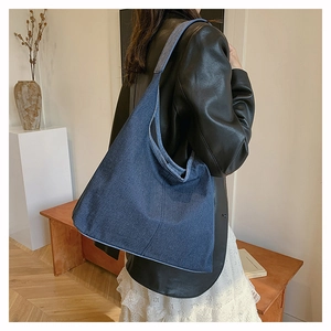 Détail d'un grand sac cabas en denim bleu foncé porté à l'épaule pour un style décontracté