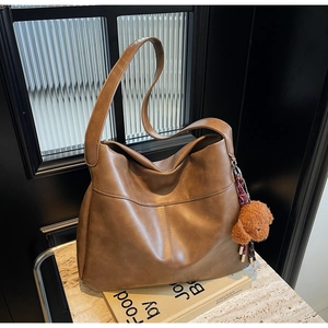 Brown faux leather tote bag with wide strap and cute teddy bear charm on marble table
