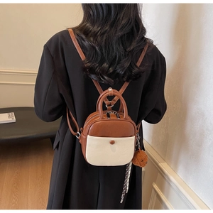 Detailed back view of a mini two-tone leather backpack with bear charm and silk scarf