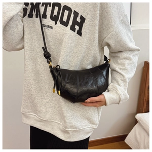 Detail shot of black shiny leather croissant bag with knotted strap and gold hardware