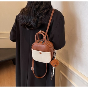 Detail of two-tone crossbody bag with plush bear charm and checkered scarf accessory