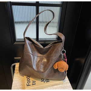Detail of dark brown faux leather tote bag with plush dog charm and woven strap