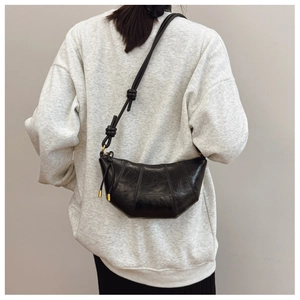 Detail of glossy black dumpling bag featuring a decorative knot strap and pleated leather
