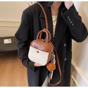 Detail of a brown and beige PU leather crossbody bag featuring a cute teddy bear charm