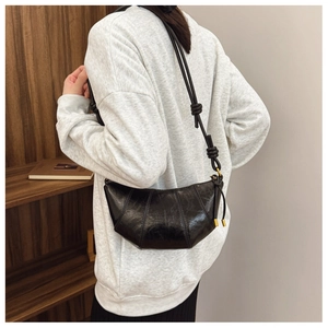 Detail of black glossy leather croissant bag showing curved stitching and gold zipper pull