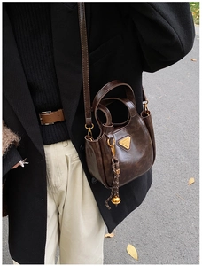 Macro detail of dark brown retro leather bucket bag with golden triangle logo and tassel