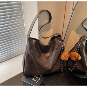 Detail of dark brown faux leather tote bag with a plush dog charm in a home setting