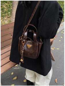 Detail view of a vintage dark brown bucket bag with a golden triangular plaque and woven charm