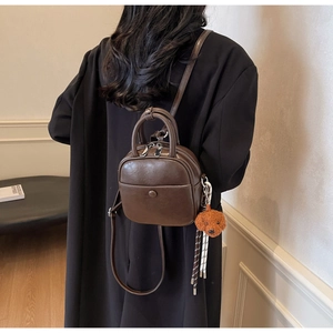 Brown mini PU leather backpack shown from behind on a model wearing a black coat