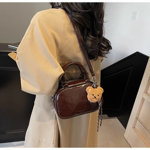 Sac bowling rétro marron brillant avec breloque ours sur un trench-coat classique