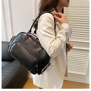Close-up of a black glossy shoulder bag with multiple silver zipper pockets on a white blazer