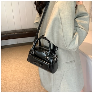 Detailed view of a black glossy Boston bag with bow accent worn over an olive blazer