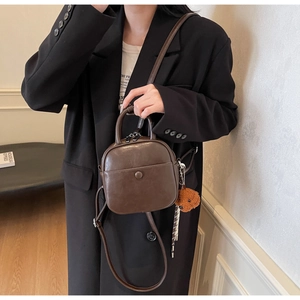Detail of vintage brown leather handbag with plush charm and adjustable strap shown on model