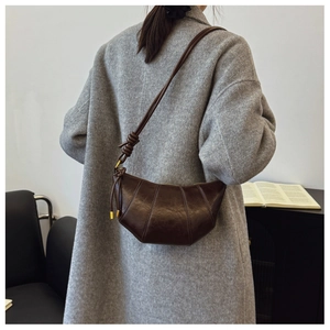 Detail of dark brown leather croissant bag featuring knotted shoulder strap and stitched segments