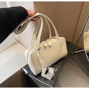 Close-up of cream rectangle handbag featuring dual handles and mini square pouch charm