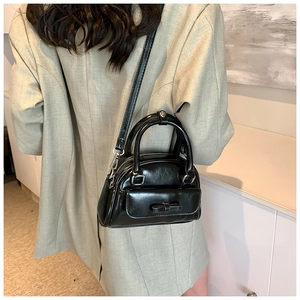 Detail of black glossy Boston bag with bow pocket and silver hardware on model