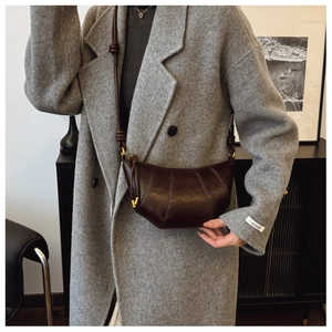 Detail of a dark brown glossy leather crescent bag with radial stitching on a wool coat