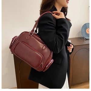 Detail of burgundy Boston bag with multi-zipper pockets shown on model shoulder