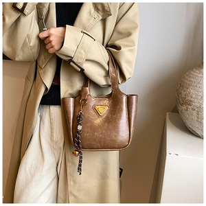 Detail of dark brown vintage bucket bag with metal logo and woven bell charm accessory