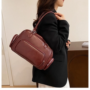 Detail of burgundy patent leather Boston bag featuring multiple utility zipper pockets