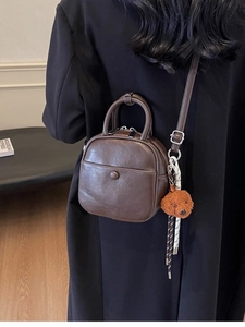 Vintage dark brown crossbody bag with handle and plush charm, shown on shoulder