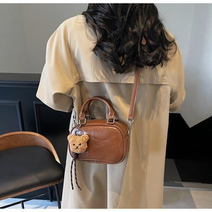 Détail d'un sac vintage en cuir marron avec un charm ours en peluche et une bandoulière