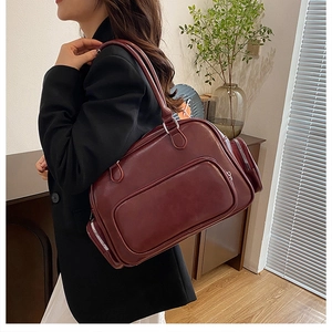 Detail view of large burgundy faux leather shoulder bag with zipper pockets worn by model