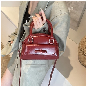 Detail of dark red patent leather Boston bag with bow accent and detachable strap