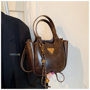 Detail of vintage brown oil-wax leather bucket bag with golden triangle logo and woven charm