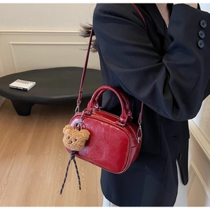 Détail d'un sac bowling en cuir rouge avec breloque ours porté par un mannequin