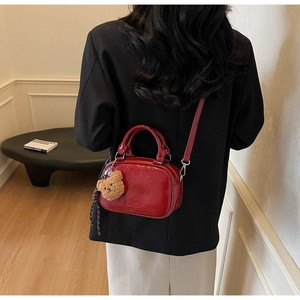 Détail du sac à main rouge brillant avec breloque ours porté par un mannequin en blazer noir