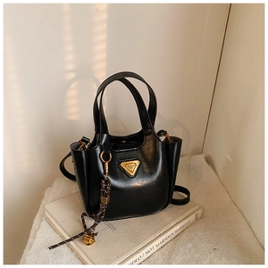 Detail of black vintage bucket bag featuring a gold triangle logo and woven bell tassel