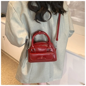 Detail of a red patent leather Boston bag with bow accent worn by a model
