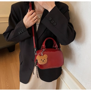 Détail d'un sac bowling en cuir verni rouge foncé brillant avec un charmant ours en peluche